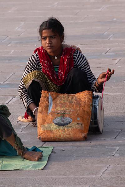 Young woman sitting on stone pavement with a sack and small drum in Rajasthan, India Pushkar, India